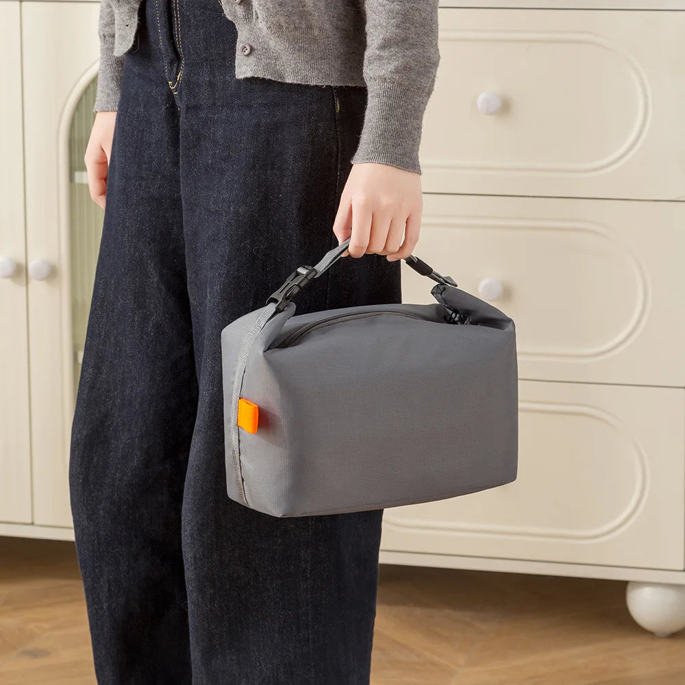 Person holding a gray toiletry bag with an orange tag in front of a beige cabinet.