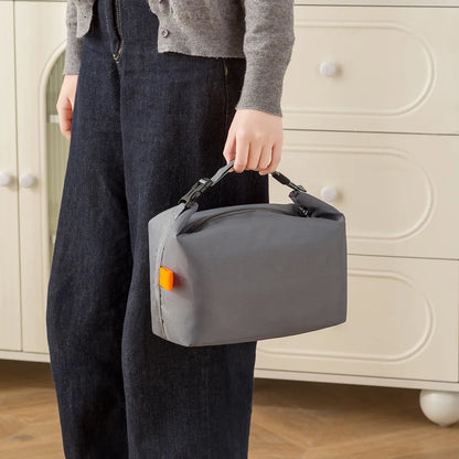 Person holding a gray toiletry bag with an orange tag in front of a beige cabinet.