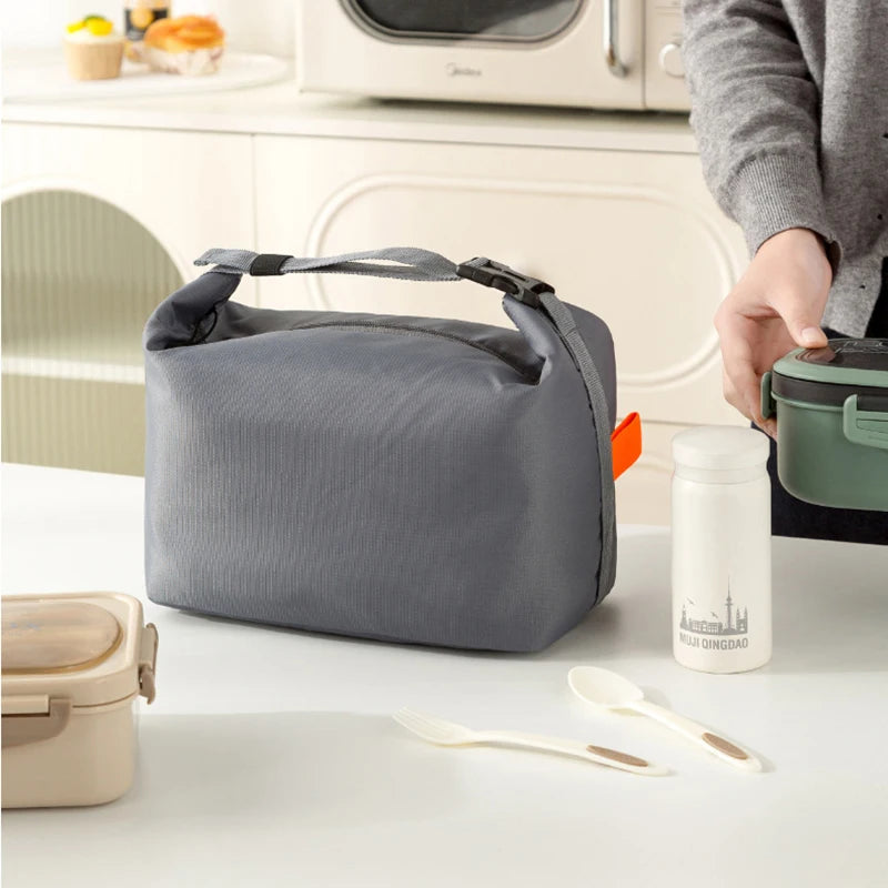 Gray lunch bag on a kitchen counter with a person and food containers in the background